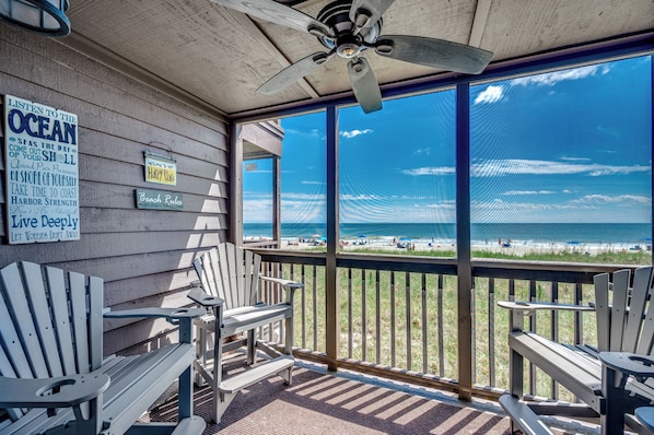 Eine überdachte Terrasse mit Adirondack-Stühlen und Blick auf den Strand.