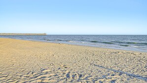Ein sandiger Strand mit einem Steg, der sich ins Wasser erstreckt.