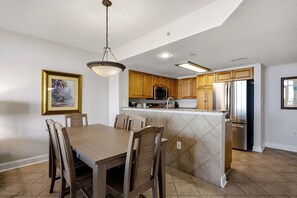 A kitchen with wooden cabinets, a central island, stainless steel appliances, and a dining area with a table and chairs.