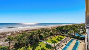 Een resort met een zwembad, palmbomen en uitzicht op het strand.