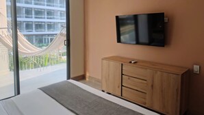 Una habitación de hotel moderna con un gran ventanal corredero que da a un balcón, un televisor de pantalla plana montado en la pared y un mueble de madera.