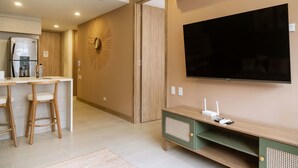 Una cocina moderna con refrigerador, taburetes de bar, televisor y mueble de entretenimiento verde.
