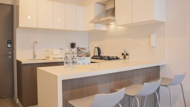 A modern kitchen with white cabinets, a central island with bar stools, a gas stove, and a kettle. - w Cozy 2BR w Balcony in Miraflores (Lima)