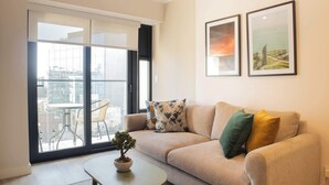 A modern living room with a beige sofa, a small round table with a plant, and a large sliding glass door leading to an outdoor seating area. - w Cozy 2BR w Balcony in Miraflores (Lima)