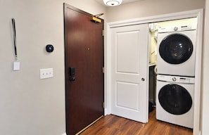 Une buanderie équipée de deux machines à laver superposées, une porte avec une poignée dorée et un thermostat fixé au mur.