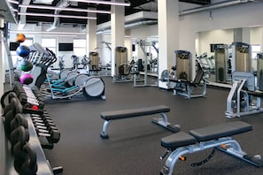 Une salle de sport équipée de divers appareils d’exercice, notamment des haltères, des bancs et des machines de musculation.