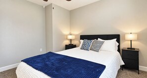 A bed with a blue blanket, two patterned pillows, and two bedside lamps on black nightstands.
