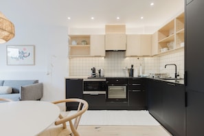 A modern kitchen with black cabinets, a built-in oven, and a dining area with a round table and chairs. - Beautifully Curated 2BD Flat, Heart of East London (Greater London)