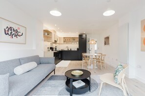 A modern living room with a grey sofa, a coffee table, and a dining area with a table and chairs. - Beautifully Curated 2BD Flat, Heart of East London (Greater London)