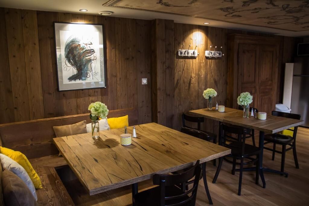 Un comedor de madera con una mesa grande y bancos, una obra de arte enmarcada en la pared y una lámpara moderna.