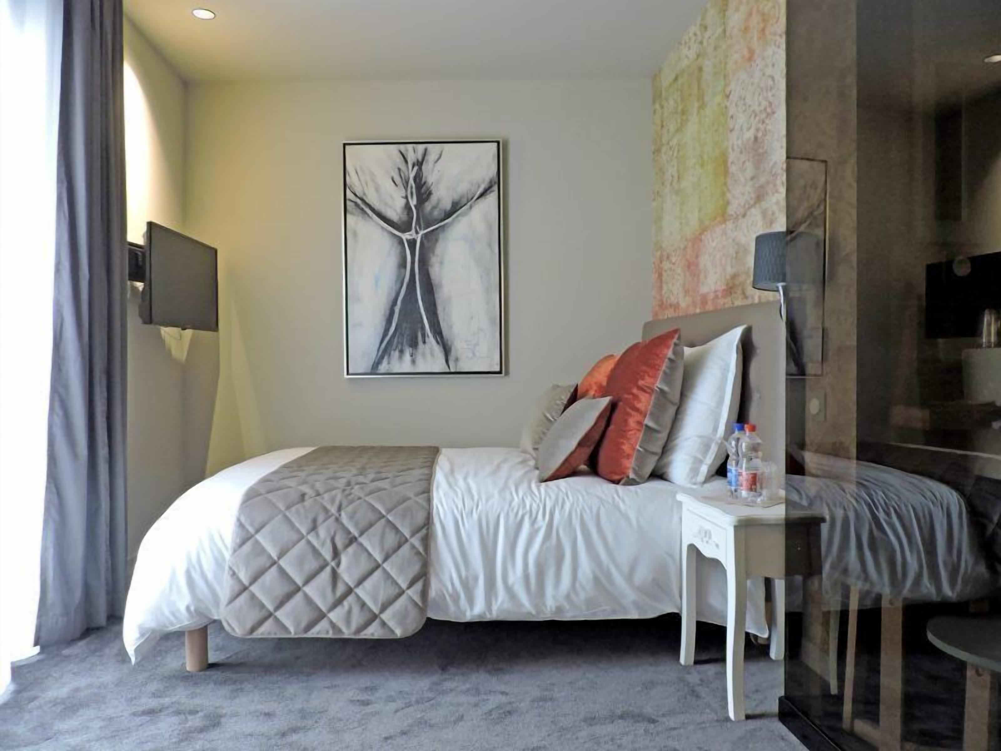 A modern bedroom with a bed, bedside table, and a large abstract painting on the wall.