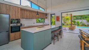 A modern kitchen with a large island, built-in appliances, and a view of the outdoor pool area. - Eko Savannah by MJ Holidays (Tamarin)