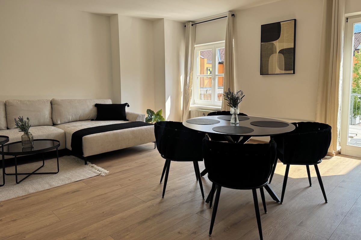 A modern living room with a sofa, a round dining table with chairs, a coffee table, and a potted plant.