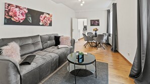 Un salon moderne avec un canapé gris, une table basse en verre et un coin repas comprenant une table et des chaises blanches.