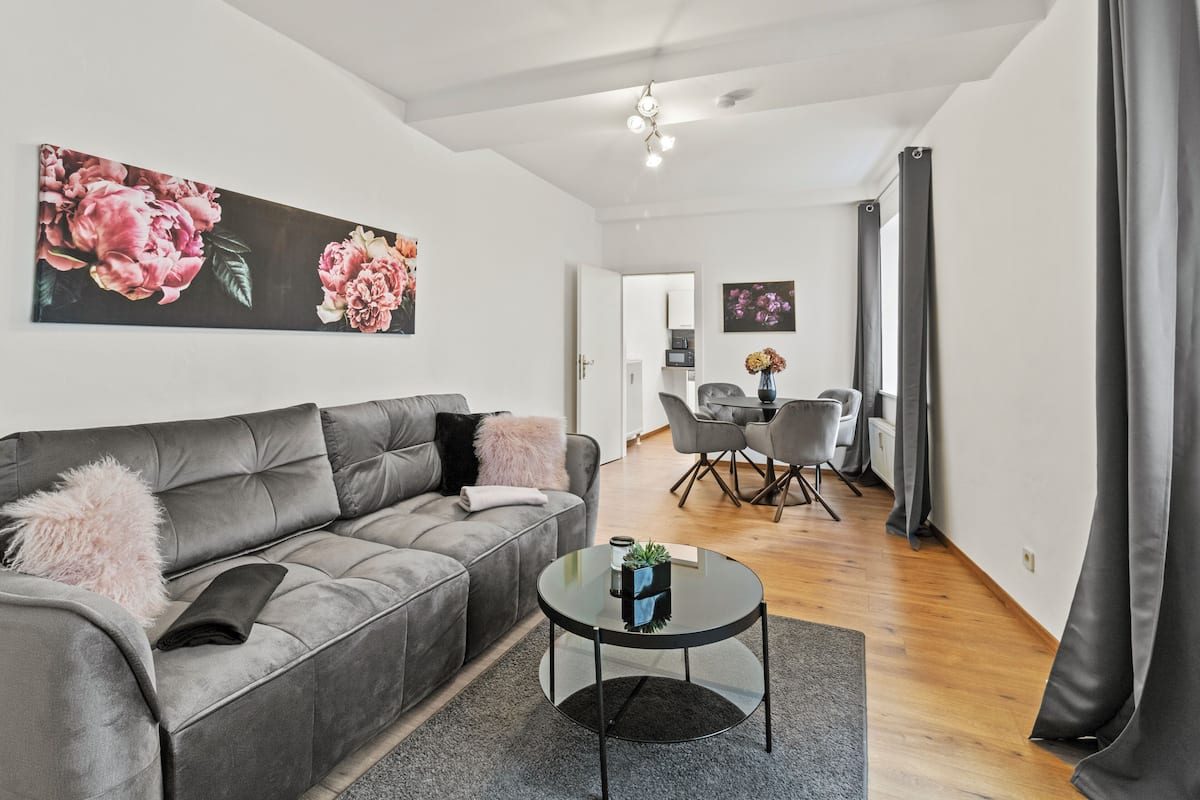 A modern living room with a grey sofa, a glass coffee table, and a dining area with a white table and chairs.