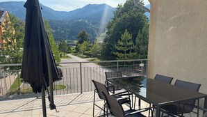 Un balcon avec une table et des chaises, donnant sur une route et des montagnes.