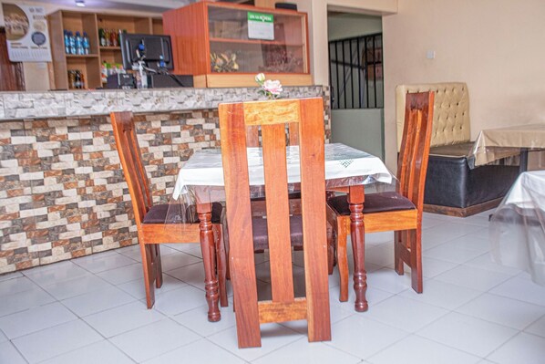Un comedor con una mesa y sillas de madera, un salpicadero de azulejos y una encimera con una exhibición de agua embotellada y otros artículos.