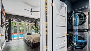 A modern bedroom with a bed, a ceiling fan, and a view of a swimming pool. - Beach Pop - Steps to Beach, Heated Pool & Hot Tub (Fort Lauderdale)