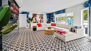 A modern living room with a patterned floor, a white sofa with red cushions, a round coffee table, and a large abstract painting on the wall. - Beach Pop - Steps to Beach, Heated Pool & Hot Tub (Fort Lauderdale)