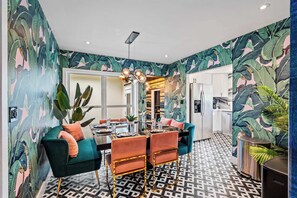 A dining area with a modern chandelier, a teal sofa, and a patterned wall. - Beach Pop - Steps to Beach, Heated Pool & Hot Tub (Fort Lauderdale)
