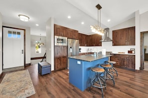 A modern kitchen with wooden cabinets, stainless steel appliances, and a blue island with stools.