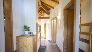 Un couloir en bois avec un sol carrelé, une petite armoire en bois ornée d’une plante, et une porte donnant sur une autre pièce.