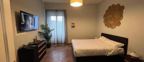A bedroom with a bed, a TV, a desk, a potted plant, and a decorative wall piece.