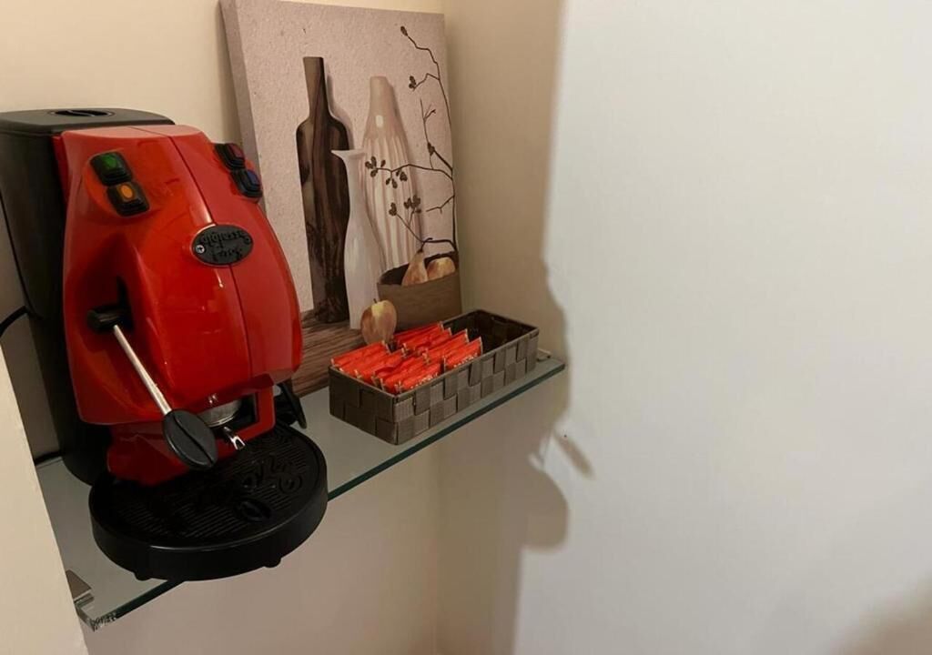 A red coffee machine on a glass shelf with a painting and a basket of bread.