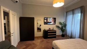 Una habitación de hotel con una cama, televisión, cómoda, espejo, planta y una puerta que da a un armario.