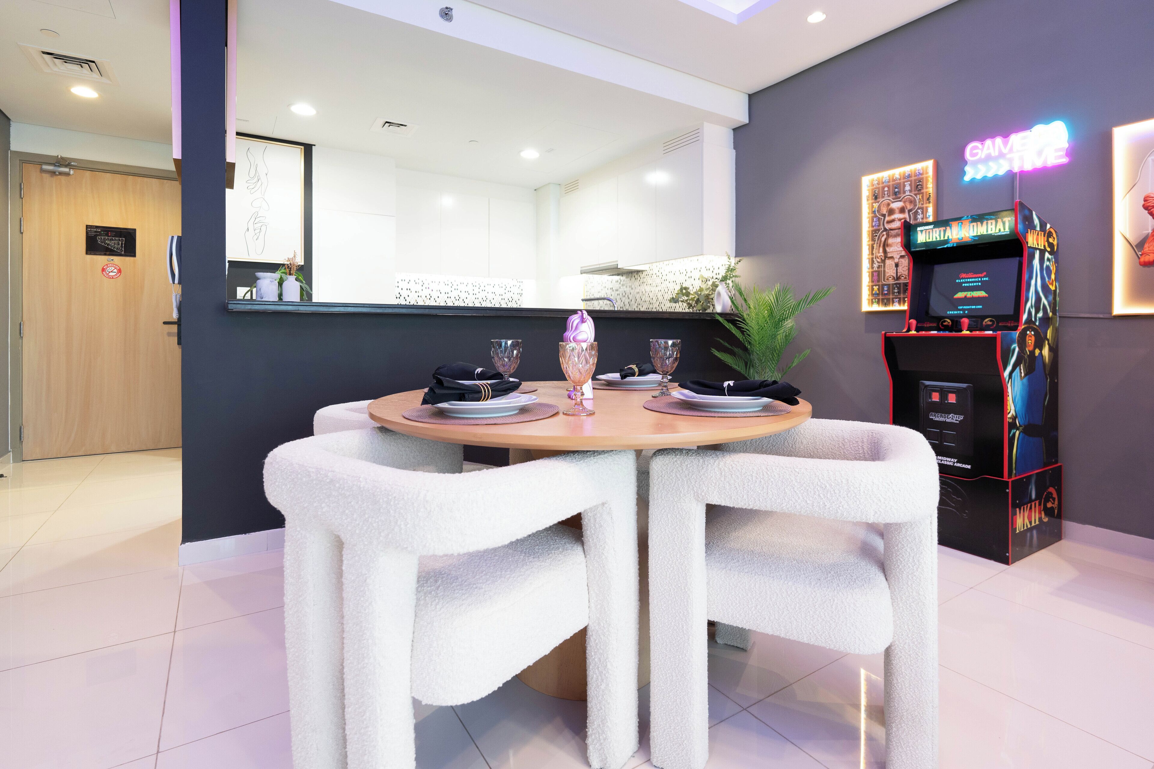 Een moderne eetruimte met een ronde tafel voor twee personen, witte stoelen en een neonbord op de achtergrond.