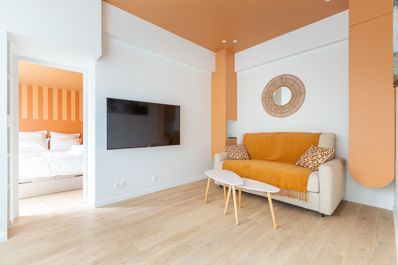 A modern living room with a flat-screen TV, a sofa with patterned cushions, and a round mirror on the wall.