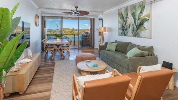 A spacious living area with a wooden dining table, a green sofa, and a large window offering a view of the outdoors. - Lago Vista on the Forster lakefront (Forster)