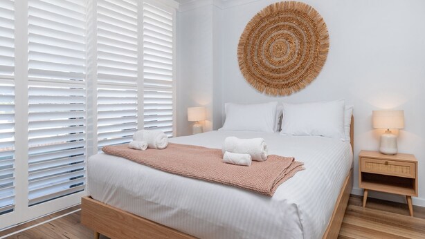A neatly arranged bedroom with a large bed, two bedside tables, and a circular woven wall decoration. - Lago Vista on the Forster lakefront (Forster)