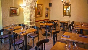 Un restaurant avec des tables et des chaises en bois, des murs en pierre et des œuvres d’art encadrées.