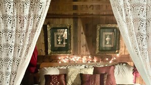 A bed with white bedding, a ruffled skirt, and a headboard with framed pictures and string lights. - Moonlight Creekside Honeymoon Adult Only Cabin accepts small pups up to 20 lbs (Sautee Nacoochee)