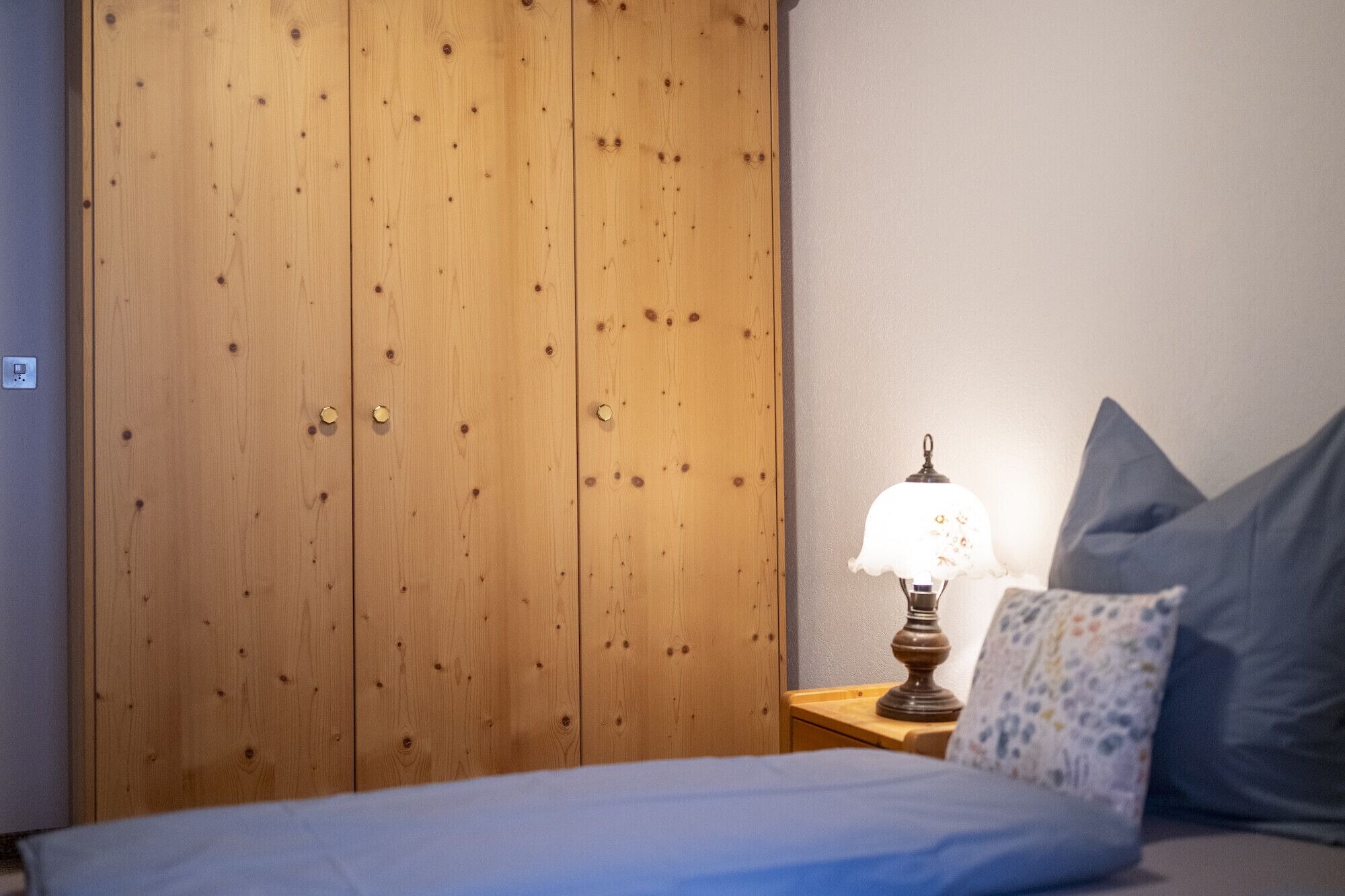 Et soveværelse med et træskab, et natbord med en lampe og en seng med puder.