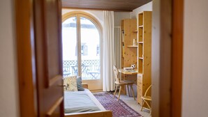 A bedroom with a bed, a desk, and a chair. There is a window with curtains and a view of a balcony. - Chasa Bügliet: Holiday flat in the village center of Sent (Sent)