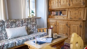 A living room with a floral sofa, a wooden cabinet with multiple drawers, and a small table with a QR code and some papers. - Chasa Bügliet: Holiday flat in the village center of Sent (Sent)