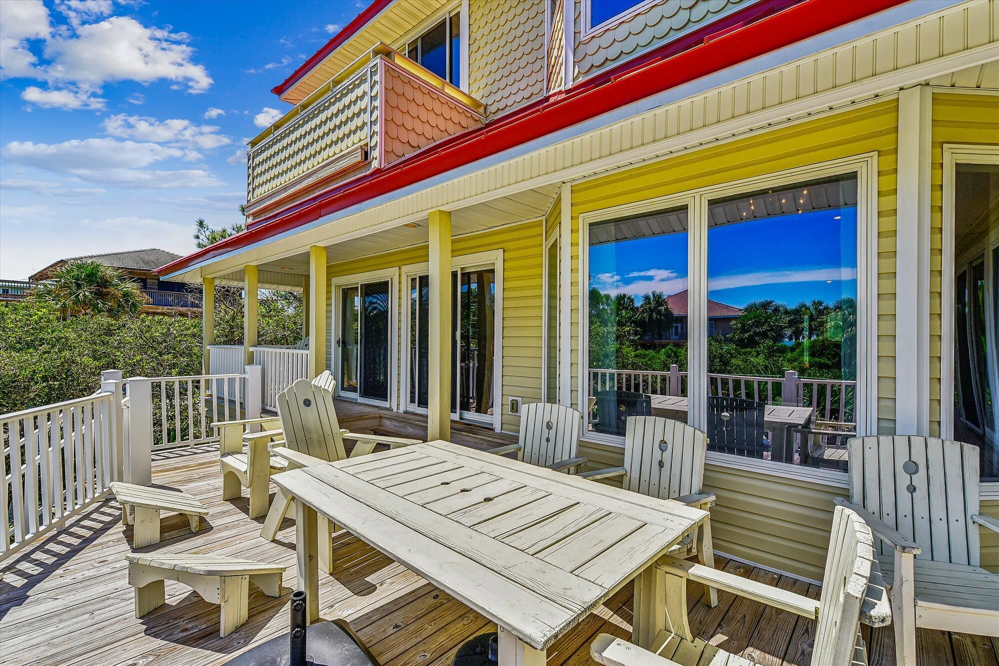 A wooden deck with outdoor furniture, a covered patio area, and large windows offering views of the surrounding landscape.