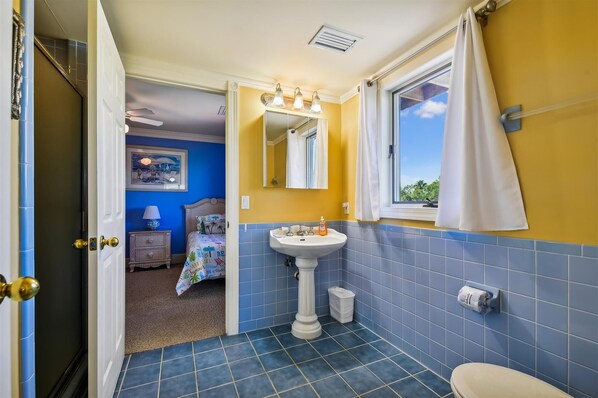 Une salle de bain avec un lavabo sur colonne, une fenêtre avec un rideau et une porte donnant sur une autre pièce.