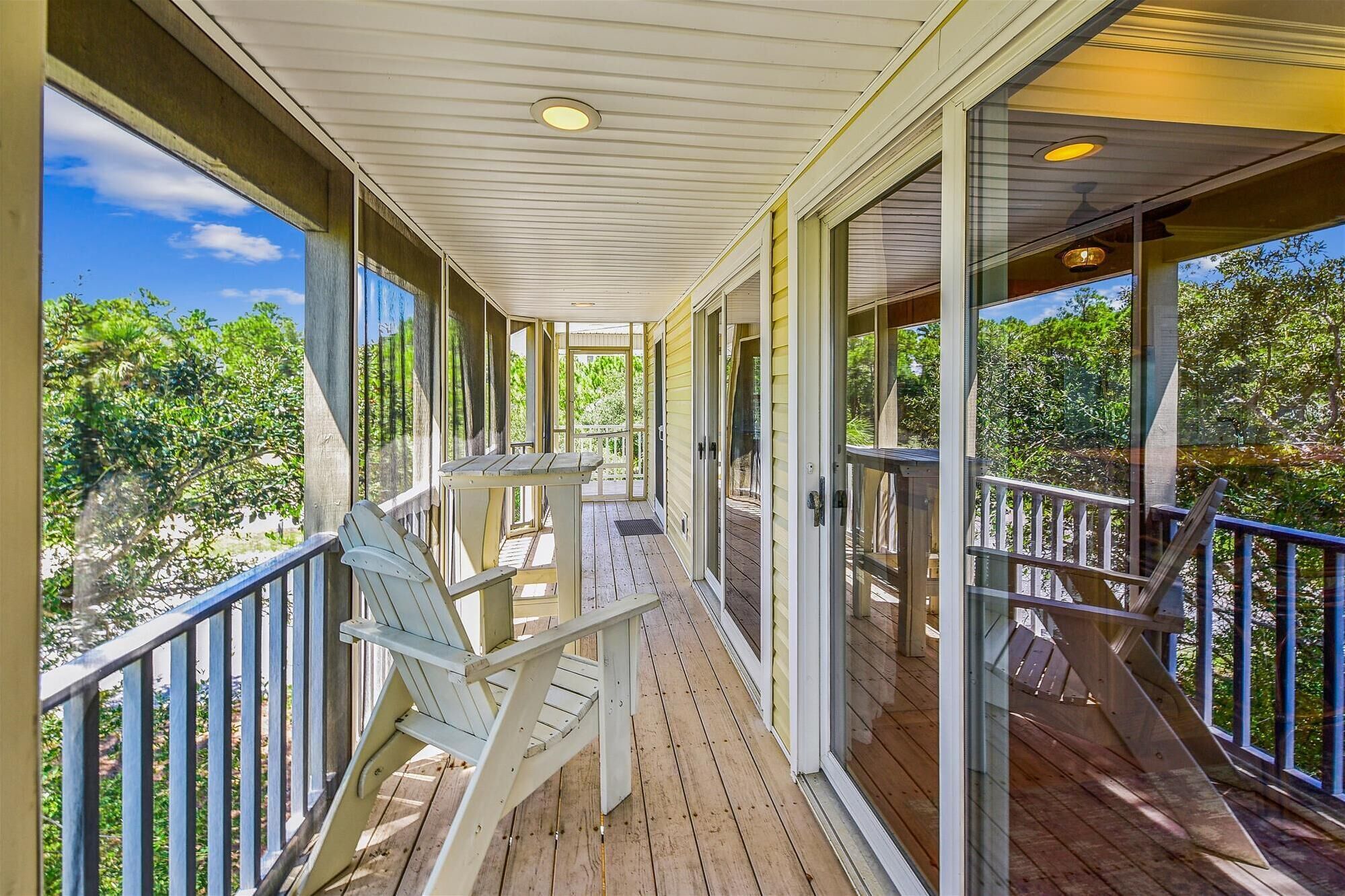 A covered porch with a wooden deck, a table, and two Adirondack chairs.