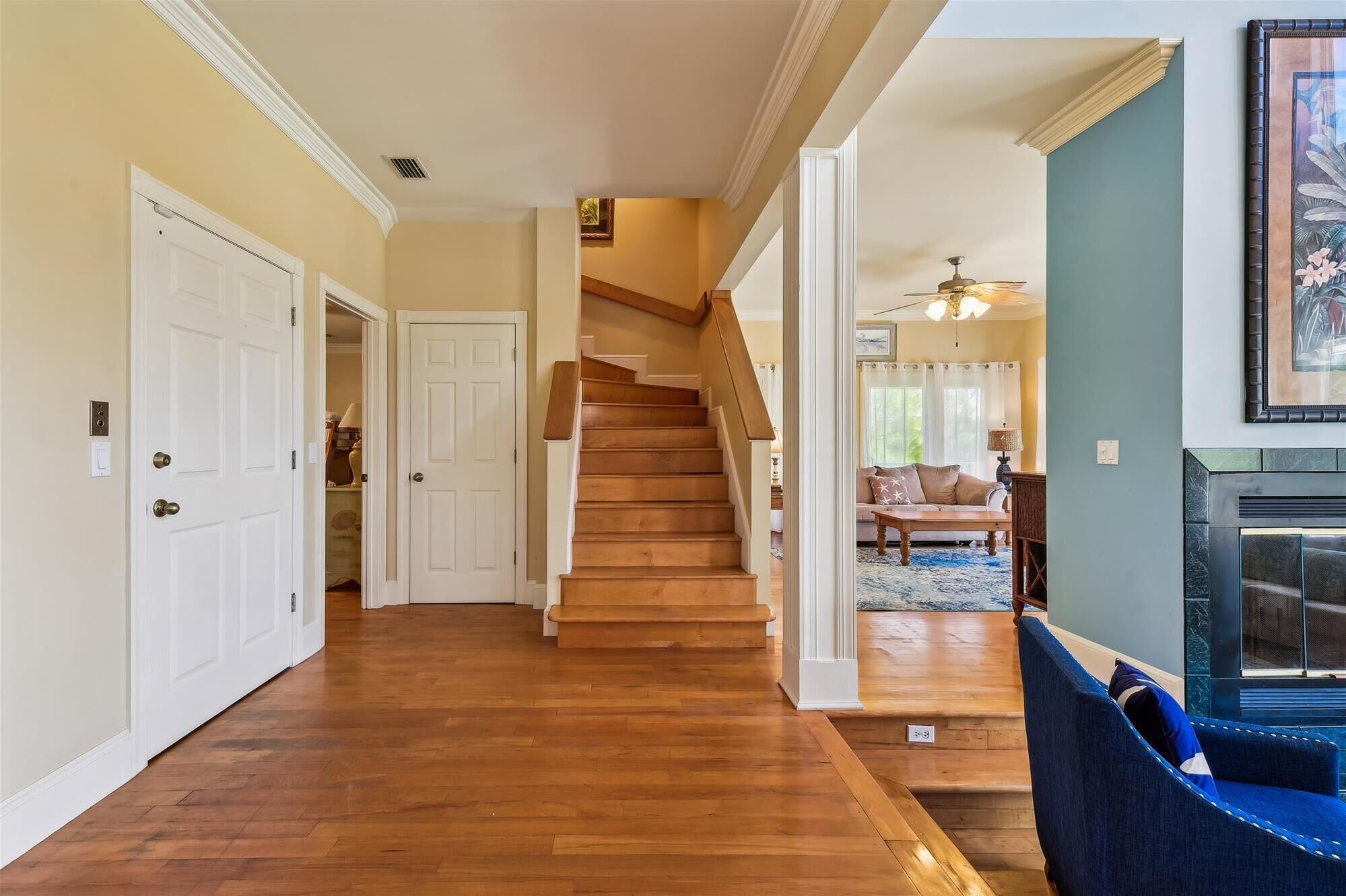 A hallway with wooden flooring, white doors, and a staircase leading to a living area with a fireplace.