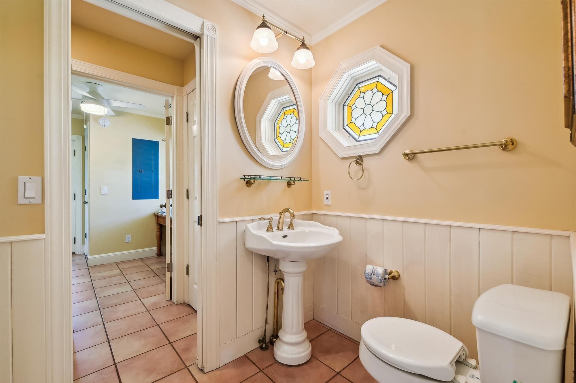 A bathroom with a pedestal sink, a toilet, and two wall-mounted mirrors with stained glass designs.