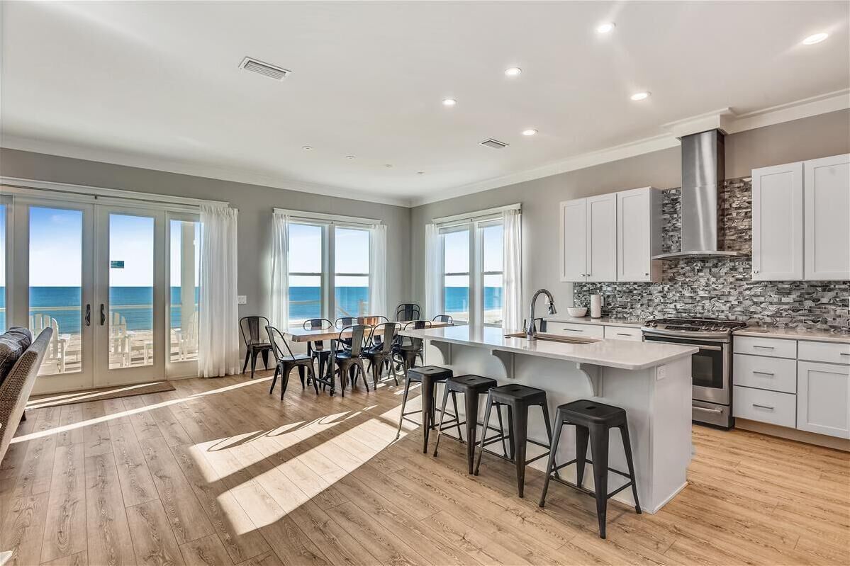 A spacious kitchen with a large island, white cabinetry, and a stone backsplash.