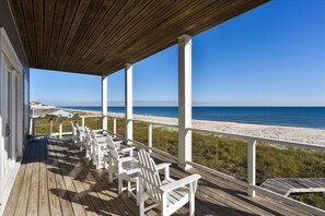 A wooden deck with white chairs overlooking a beach.