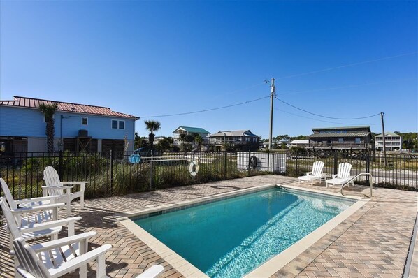 A swimming pool with lounge chairs, surrounded by a fence, and houses in the background.