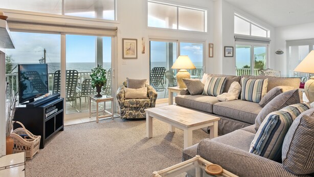 A spacious living room with a large television, comfortable seating, and a view of the ocean.