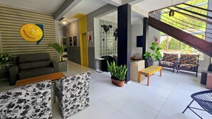 A modern living room with a sofa, a coffee table, and a patterned ottoman. There is a staircase leading to an outdoor area with a view of greenery. - Foresthouse Beach Hostel (Florianópolis)