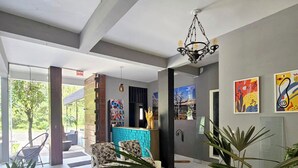 A spacious living area with a modern design, featuring a large sofa, a coffee table, and a chandelier. There are several pieces of artwork on the walls and a variety of plants. - Foresthouse Beach Hostel (Florianópolis)