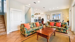 A living room with two floral-patterned sofas, a wooden coffee table, and a kitchen in the background.